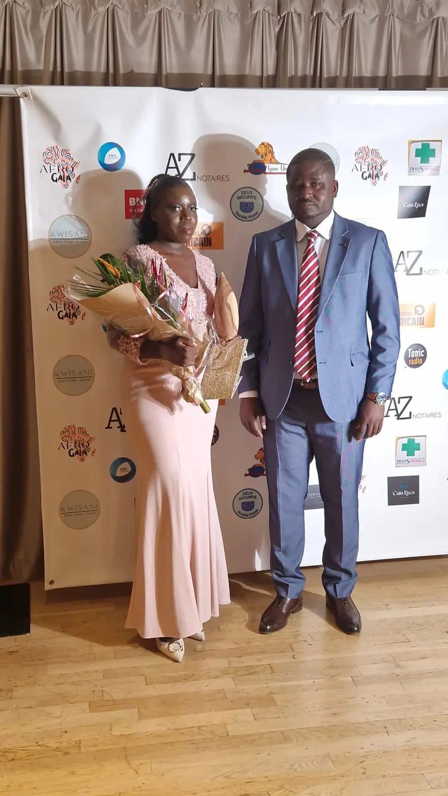 Deux invités devant le mur des partenaires à l’Afro Gala 2023, aux Terrasses du Parc à Villeurbanne